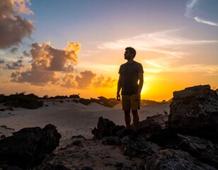 Fototapeta premium Man standing on rocks watching the sunset with beautiful orange and yellow colors in the sky.