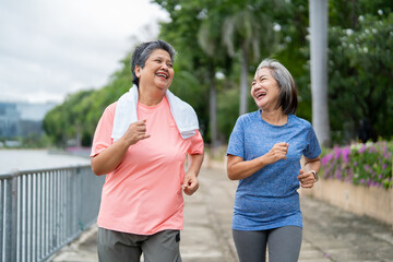 Two happy Asian senior women jogging exercise outdoors in modern city.