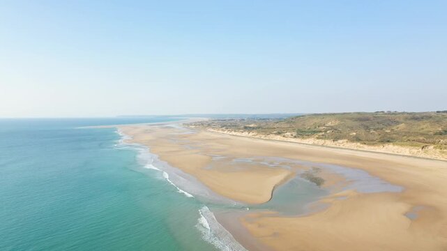 Wide aerial shot of Plage de la Vieille eglise with turquoise sea, sandy shoreline, and gentle waves under a clear sky. Natural coastal landscape with dunes and tidal pools.