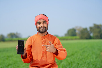 Fototapeta premium Young indian farmer showing smartphone screen at agriculture field