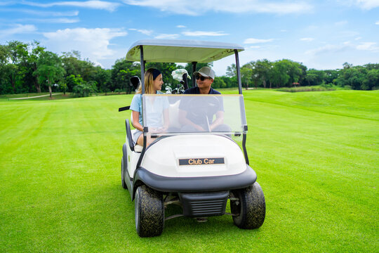 Asian golfer team ride in golf cart together on a scenic golf course.