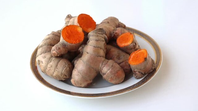 Close-up of fresh organic turmeric rhizomes and vibrant sliced roots on a plate. Natural curcumin source for healthy cooking and herbal medicine. High-quality ingredient for wellness and detox