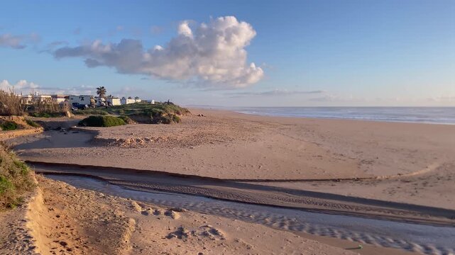 Sandy Rota beach landscape showing a small stream flowing across the sand into the Atlantic Ocean under a blue sky