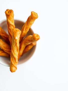 Close-up top-down view of golden fried dough sticks in a white bowl,  baked,  cakwe