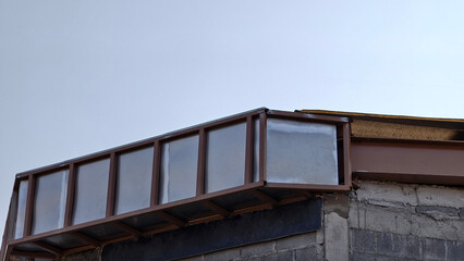 Fototapeta premium Close-up of brown metal roof framework and steel panels installed on grey concrete block wall. Shows industrial construction details and architectural metalwork under pale sky