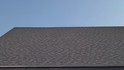 Detailed view of residential roof featuring dark grey asphalt shingles against clear blue sky. Showcases professional roofing installation texture and modern home exterior design © sutthichai