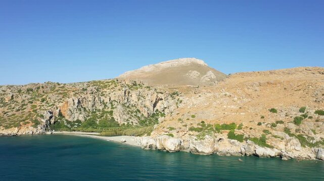 Scenic view of Preveli Beach with turquoise waters, rugged cliffs, and arid hills under a clear blue sky in Crete, Greece.