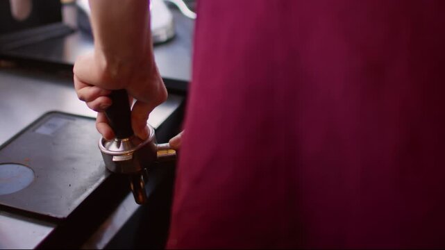Preparing espresso. Tamping coffee. Barista hand pressing fresh grinded beans powder in metal horn. Professional restaurant appliance.