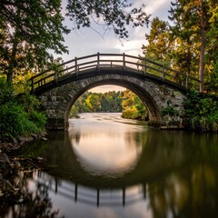 Obraz premium Picturesque Stone Bridge Spanning a Serene River Amidst Lush Greenery and Reflections.