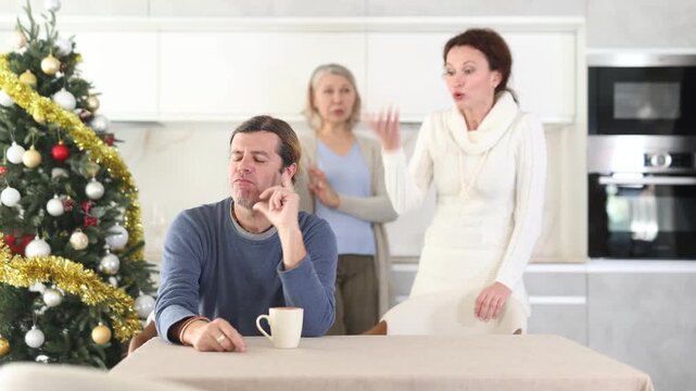 On Christmas Eve elderly mother and woman scold swear at man. Man is upset because of family conflict, dejectedly listens to his wife and mother scolding him. Complex intergenerational relationships