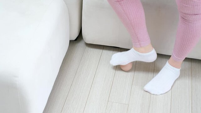 A woman's foot in white socks rolls massage ball on the floor, top view.