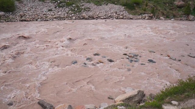 Slow motion shot of flooded Chenab river flowing in the mountains during the monsoon season after heavy rainfall as seen from Tandi village in Lahaul and Spiti district, Himachal Pradesh, India.