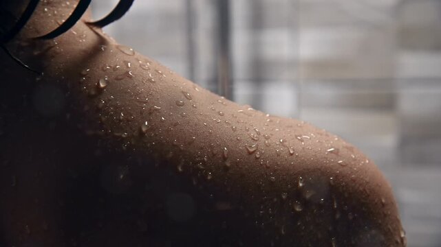 close-up of Female figure with wet skin and droplets on shoulder, illuminated by soft light in a bathroom setting with blurred tiles and shower curtain in the background