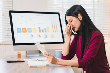 Stressed Asian business woman having headache and feeling tired holding finance paper at office...