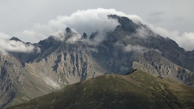Rocky Mountains fog timelapse over rugged peaks as clouds spill across alpine ridges. USA range crests in haze, swift vapor streams around jagged summits during changing weather.