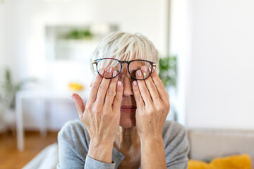 Mature woman with glasses rubbing her tired eyes at home. Eye strain, fatigue, and vision problems...