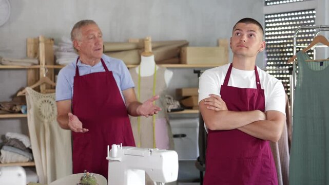 Mature tailor scolds a young assistant and emotionally pronounces dissatisfaction in the workshop. High quality 4k footage