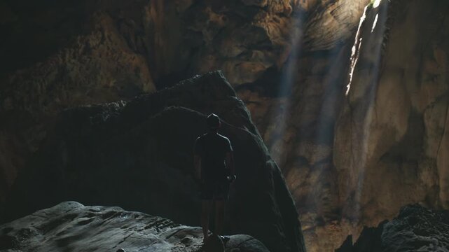 Young hiker explores majestic location of a Cave with light beaming through darkness of the cavern in Laos, Southeast Asia