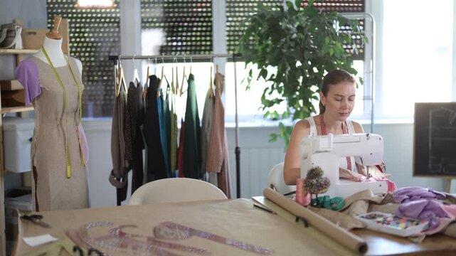 Qualified dressmaker sews clothes in the workshop. Seamstress works in a summer workshop. High quality 4k footage