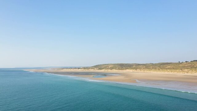 Aerial view of the expansive sandy shoreline and turquoise waters at Plage de la Vieille eglise under a clear blue sky. The tranquil coastal landscape features gentle waves and natural dunes.