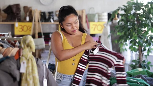 Young woman chooses fashionable sweater in a clothing store. High quality 4k footage