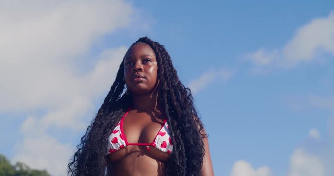 A young girl in a two-piece dipping her toes in the water while posing for a side shot.