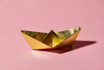 Paper boat origami sculpture made from shiny gold foil on soft pink background, minimalist studio still life with copy space, childhood play and travel concept