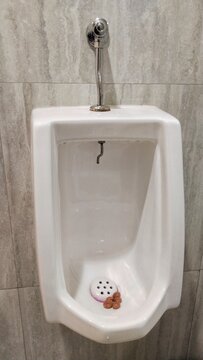 Close-up of a white ceramic wall-mounted urinal with a manual flush valve and deodorizer mothballs in a men's public restroom