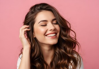 Fototapeta premium Young woman touching hair laughing joyfully against pink background portrait closeup