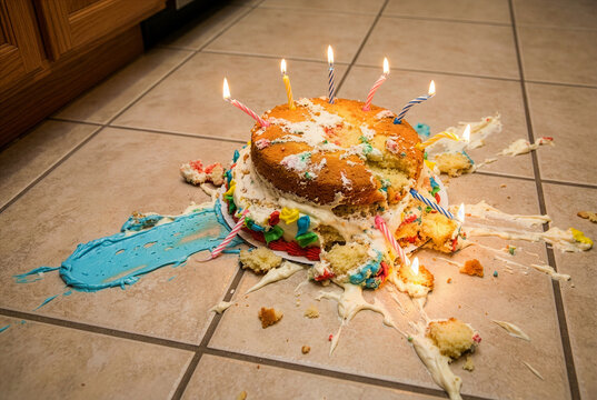 Ruined birthday cake dropped on the tiled kitchen floor with candles still burning