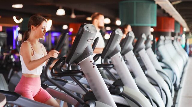 Young athletic woman in sportswear training on elliptical machine in gym 