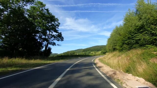 Empty country road winding through lush green hills and forests in the Morvan region under a clear blue sky. Peaceful rural landscape ideal for travel and nature concepts.