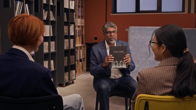 Middle-aged biracial male author showing cover and talking about his upcoming book during presentation in library