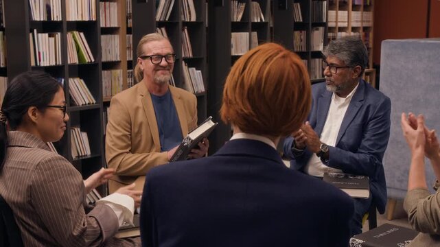 Middle-aged happy male author finishing presenting his new book during book club gathering in library