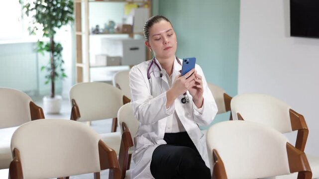 Attentive positive young girl medical student sitting and listening lecture, taking photo or QR with mobil in light lecture hall