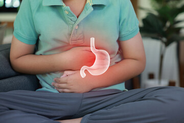 Little boy suffering from stomach ache with x-ray gastric graphic overlay, child holding belly feeling painful from indigestion, gastritis, food poisoning or abdominal pain at home.