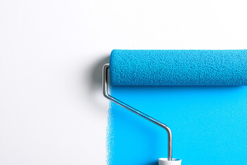Obraz premium Blue paint roller applying a fresh coat of bright blue paint on a clean white wall surface