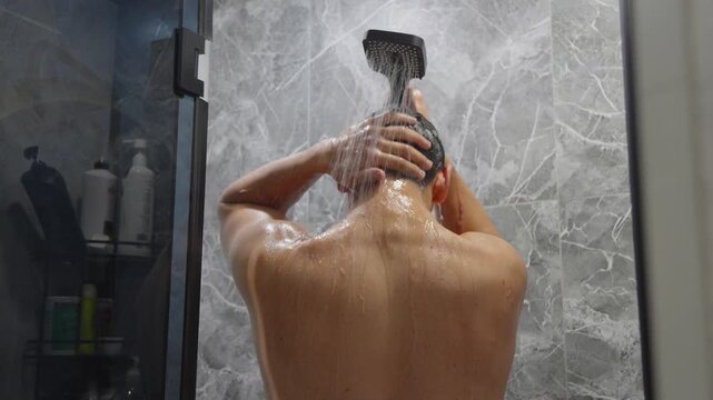 Rear view of man washing hair in the shower at home
