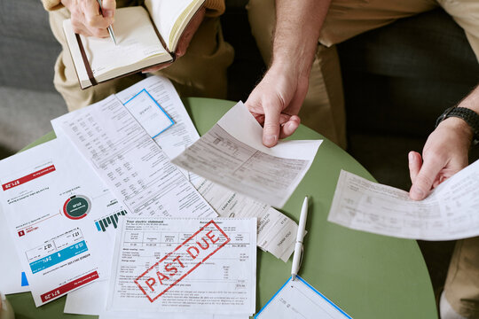 Caucasian senior man and Caucasian senior woman reviewing overdue bills and financial documents at table, holding papers with past due notice, discussing personal finances