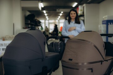 Fototapeta premium Pregnant woman choosing modern baby strollers for newborn