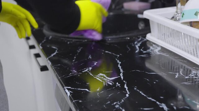 Cleaning kitchen black countertop with yellow cloth and spray