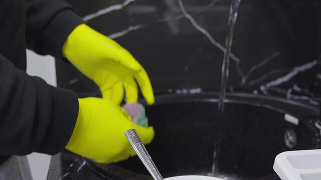 Person washing black sink in the kitchen with sponge