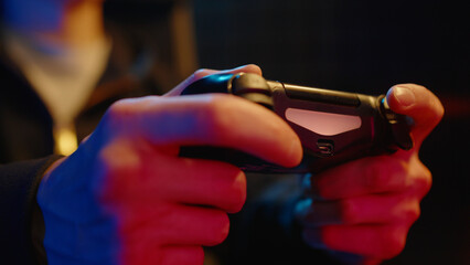 Young teen boy streamer gamer man playing online video game on computer use joystick. Gaming console virtual entertainment. Cyber e sport videogame controller. Neon light. Tense player hold joypad. © Татьяна Епанешникова