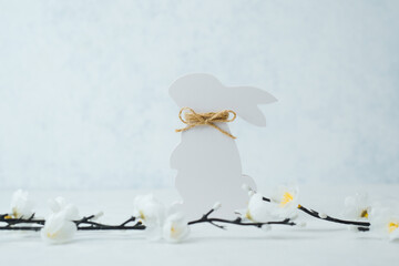 Fototapeta premium Elegant white Easter bunny cutout with twine bow and white flowers on bright background
