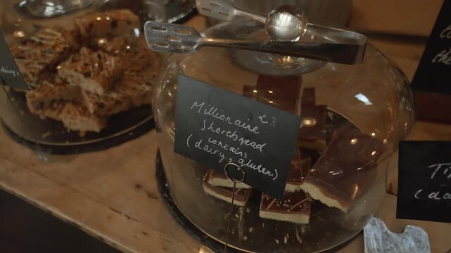 Medium close up orbit of Millionaire shortbread in glass case in farm shop, daytime.