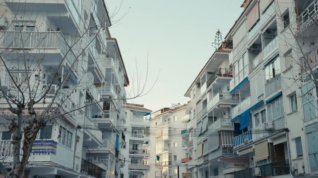Urban street view of white apartment buildings with balconies, awnings, and visible utility wires in a coastal town in southern Spain.
