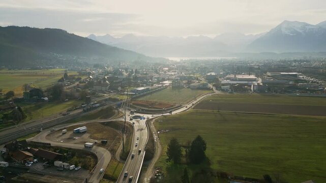 Drone shot overlooking a small town surrounded by farmland and mountains, with roads leading through open fields toward the urban area in soft morning haze.