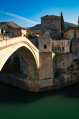 Naklejka premium Epic Mostar Stari Most bridge authentic vertical panorama. Cinematic view of historic old town, ancient stone tower, emerald Neretva river and mountains in Bosnia and Herzegovina. 