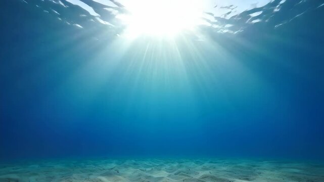 Underwater scene with sun rays penetrating the deep blue ocean water and sandy seabed