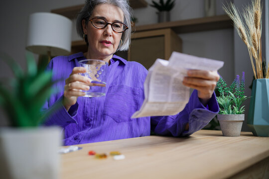 Woman reads medication instructions at home holding glass of water